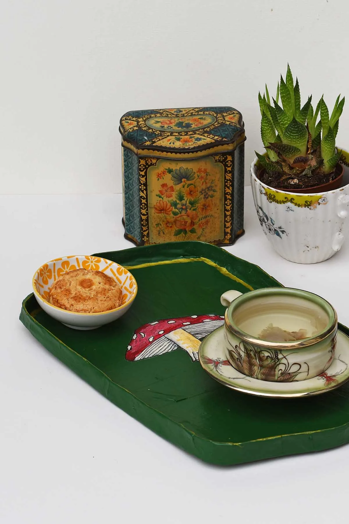 homemade mushroom paper mache tray with tea cup and treat. Plant and tea caddy in the background