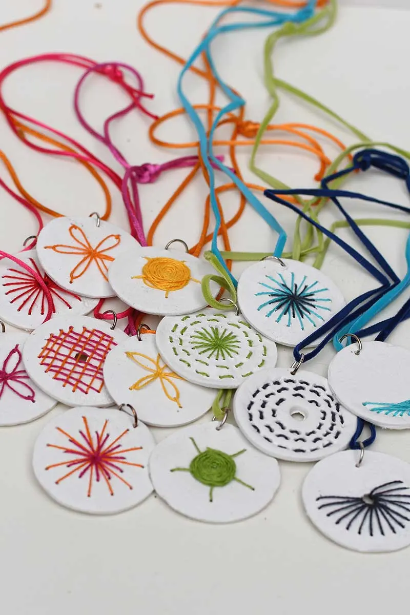 rainbow of embroidered clay necklaces on coloured thread