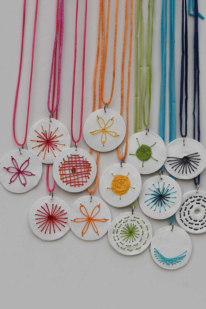 a rainbow of embroidered clay pendant necklaces hanging down.