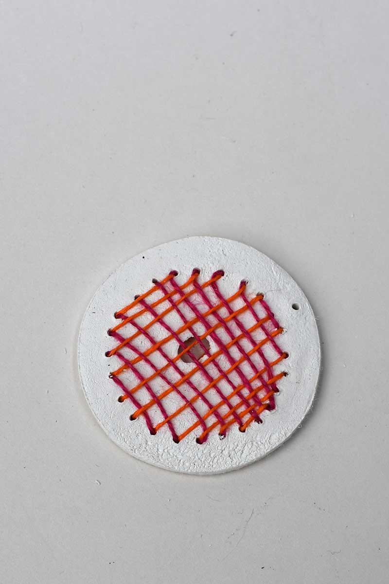 hatched woven design in pink and orange on a clay disc