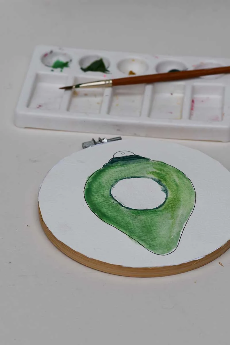 watercolour paints in green with bauble shape on watercolour paper on an embroidery hoop