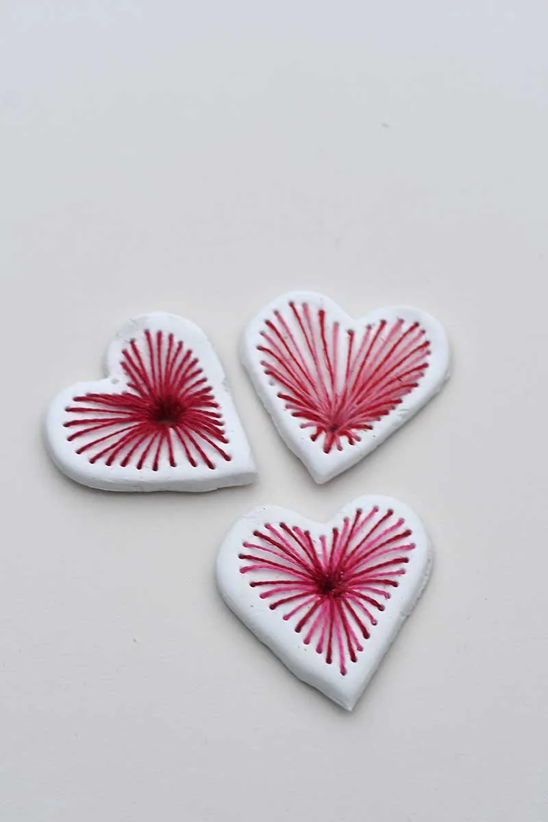 three embroidered clay heart pendants